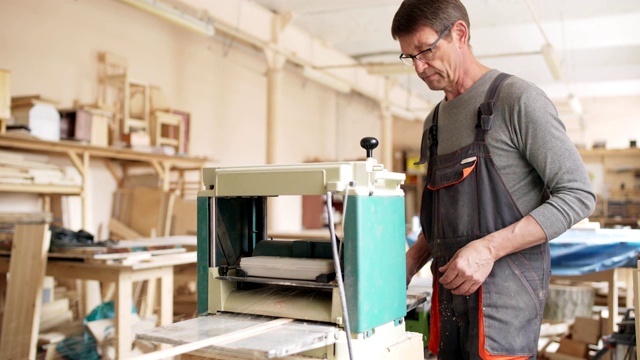 在他的家具制作工作室里，集中成熟的木工使用电动砂光机在长木板上工作视频素材