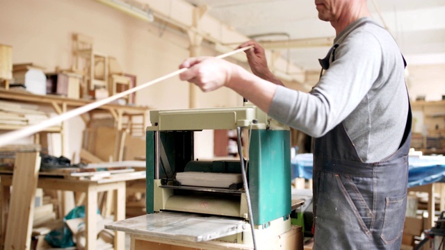 熟练成熟的家具制造者在他的工作室使用木工机器打磨长木板视频素材