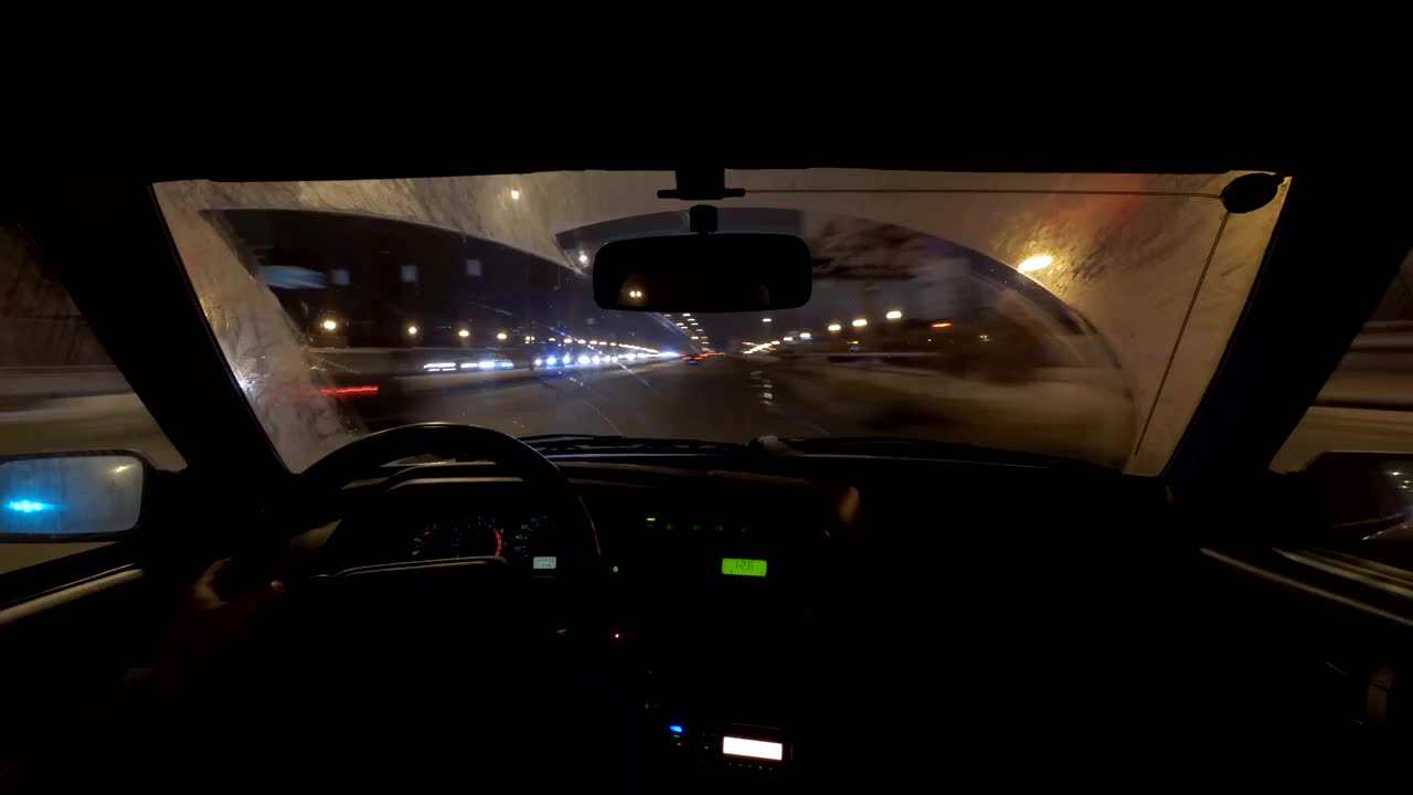 在城市的夜晚，男人坐在汽车的座位上，从控制面板和道路上观看视频下载