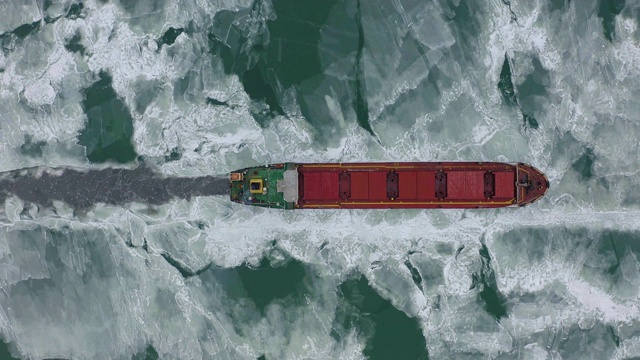 在极端冬季条件下在冰冻海面上航行的货船航拍。在破冰船造成的狭窄航道中航行。北方寒冷冬季的水运视频下载