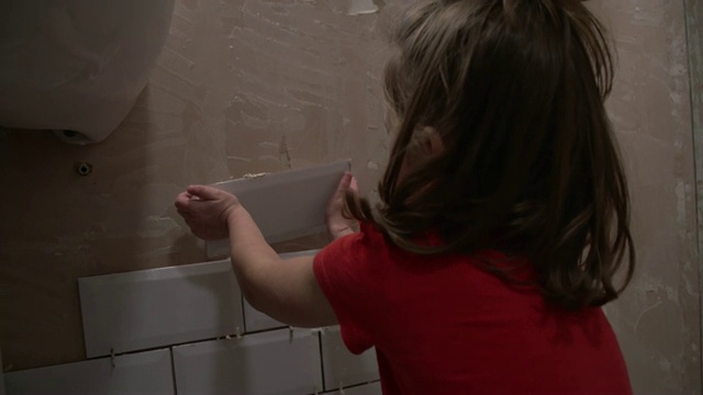 小女孩对着镜头微笑，把瓷砖贴在墙上。学习如何家居装修的理念视频素材