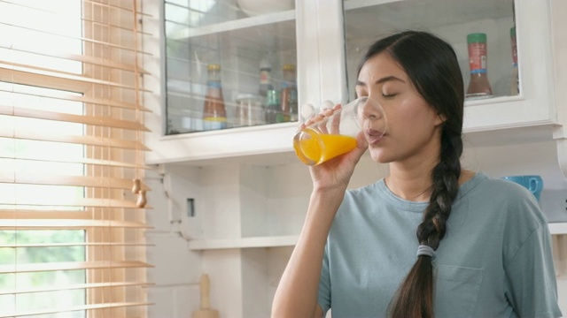 年轻美丽的亚洲女人在厨房喝橙汁的特写，健康的生活方式视频素材