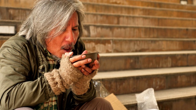 一位无家可归的老人坐在城市的楼梯上，吃着来自志愿者的汤视频下载