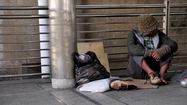 一个无家可归的老人穿着脏衣服坐在街上寻求帮助视频素材