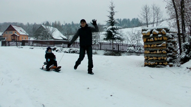 父亲和儿子享受着在乡村道路上乘坐雪橇的乐趣视频素材