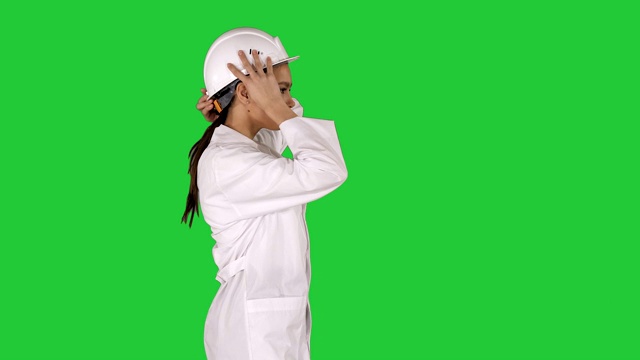 穿着白色长袍戴着安全帽的女人走在绿色屏幕上，色度钥匙视频素材