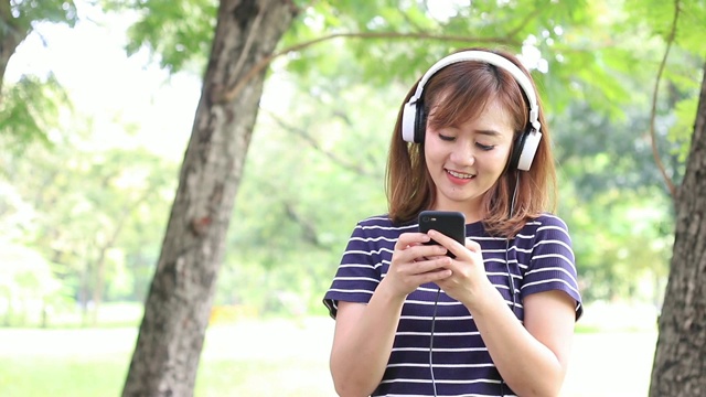 女孩在花园里用智能手机听着、享受着音乐，她是休闲日的幸福视频素材