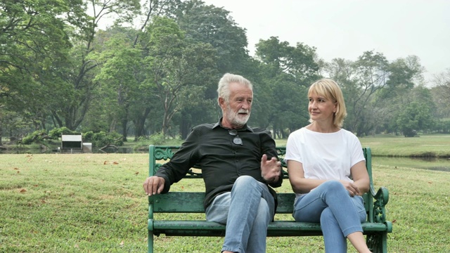 一对老夫妇在一个阳光明媚的日子里在公园里聊天。老年夫妇在森林里放松的春天夏天的时间。自由的时间，退休的生活方式爷爷奶奶的概念。慢动作视频素材