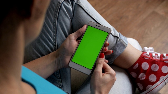 女孩在用手机。女人手里拿着智能手机的绿屏是绿屏，男人手里拿着智能手机的绿屏是色度键，背景是白色。技术的概念。视频素材