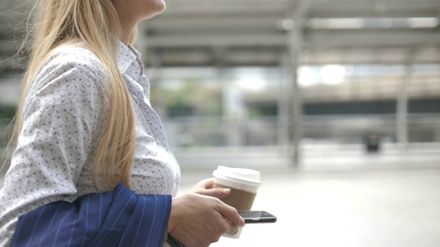 一个女人拿着智能手机和咖啡杯走在街上视频素材