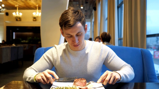 一个年轻人下班后在咖啡馆用刀叉吃美味的牛排视频素材