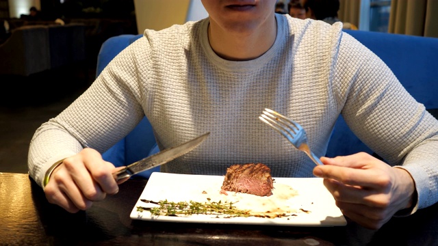 一个男人晚上在快餐店用刀叉吃牛排视频素材