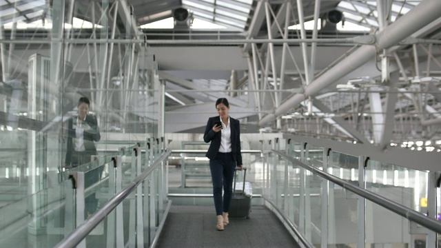 女商人在机场使用智能手机和提行李箱视频素材