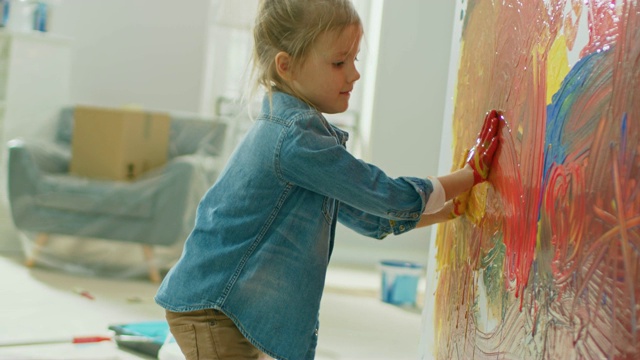 快乐的小女孩用手蘸着鲜艳的颜料在墙上画了五颜六色的抽象画。她开心地笑着。房屋正在装修。视频下载