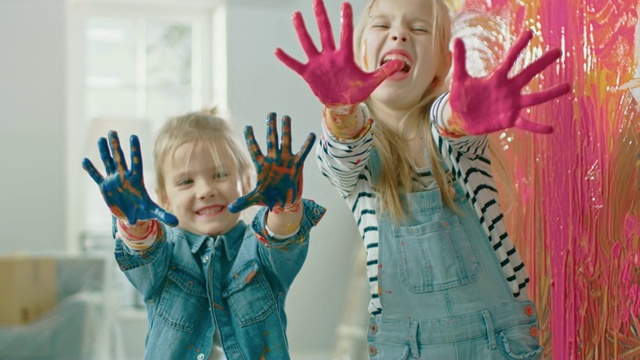两个有趣的小姐妹展示她们的手蘸了彩色颜料。他们是快乐的和笑。姐妹关系的目标。重新装饰在家里。视频下载
