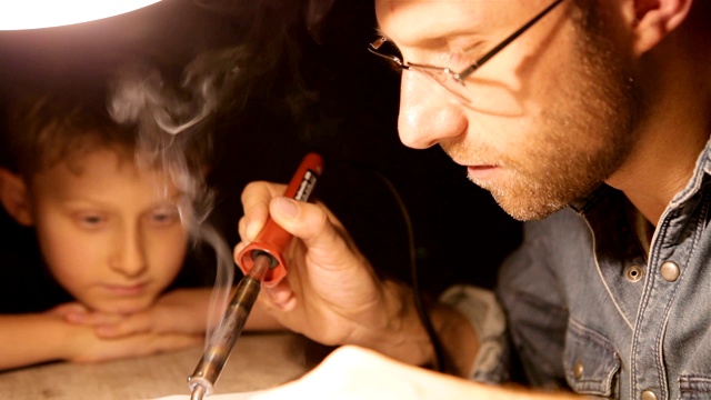 父亲和儿子一起焊接电子零件视频素材