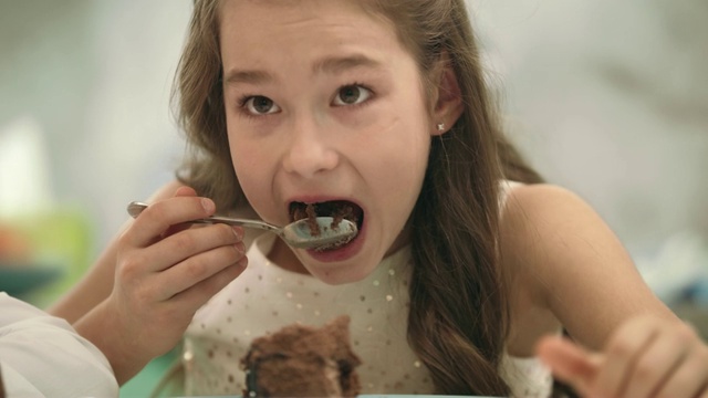 漂亮女孩在吃巧克力蛋糕。孩子吃生日蛋糕的肖像视频素材