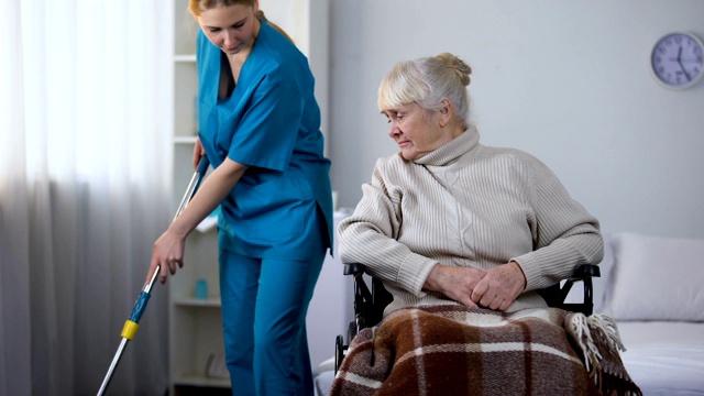粗鲁的医院看门人打扫房间，带着老女病人移动轮椅视频素材