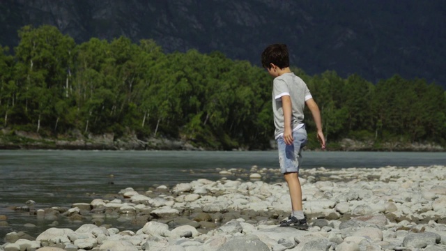 男孩在河边玩耍，把石头扔进水里视频素材