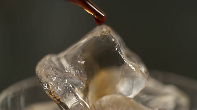微距拍摄的冰块在饮料杯和棕色鸡尾酒苦味滴从它上面的移液管视频素材