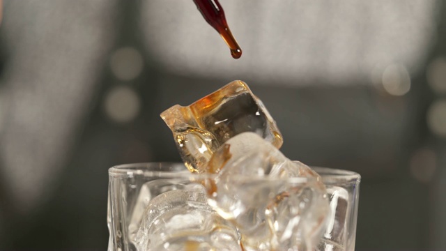 这是一个特写镜头，上面有冰块和移液管，正在滴下棕色液体鸡尾酒苦味滴。视频素材