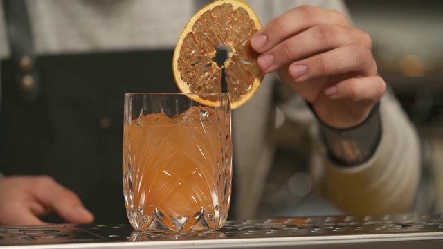 一个近距离的柚子汁的玻璃杯站在吧台和一个男人的手放在葡萄柚片的边缘视频素材