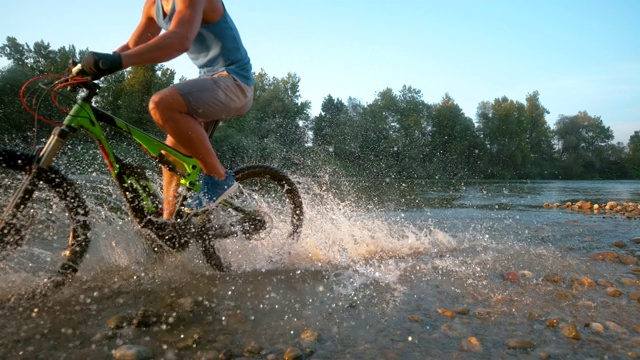 时间扭曲:阳光灿烂的夜晚，快乐的山地自行车手在浅河里骑行。视频素材
