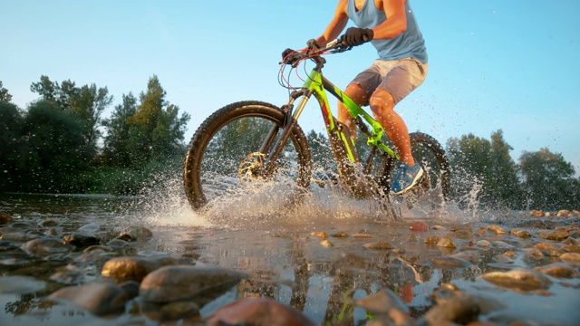 低角度:活跃的男子骑着他的山地车，溅着清新的水。视频素材