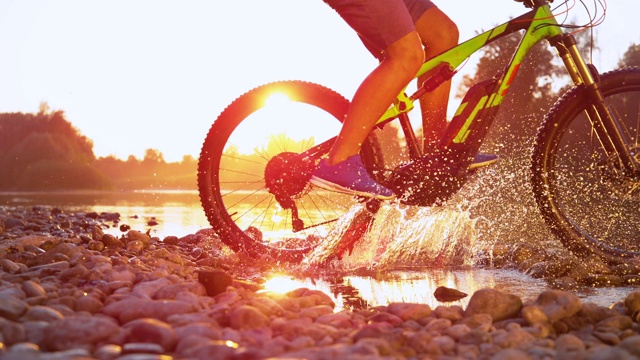 慢镜头特写在日落时，一个不认识的人在浅河上骑自行车视频素材