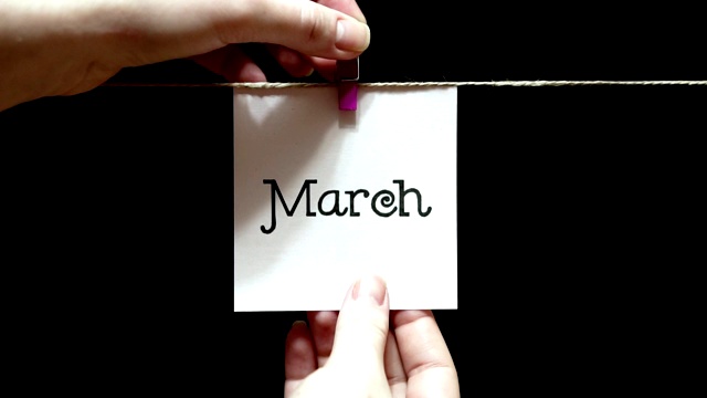 一年中的月份。春天。在纸上刻有“三月”字样。床单是用一个晾衣夹手动固定在绳子上的。黑色背景。视频下载