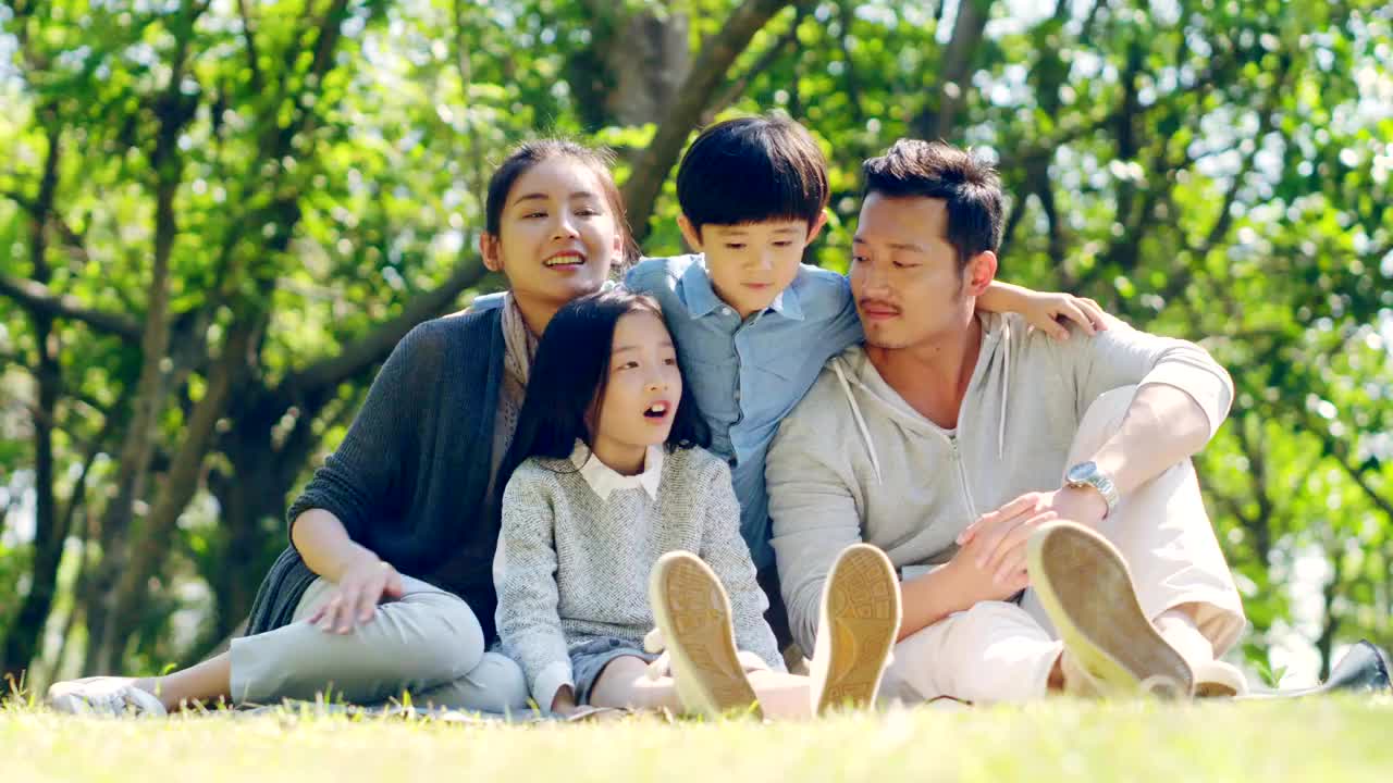亚洲家庭坐在公园户外的草地上视频下载
