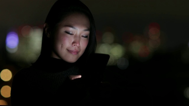 亚洲女性晚上在街上使用面部识别技术解锁智能手机视频下载