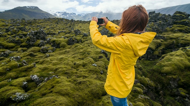 身穿黄色雨衣的游客拍摄冰岛火山景观上的苔藓覆盖视频素材