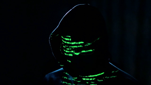 一名男性黑客在电脑上工作，绿色代码字符映入他的脸上视频素材