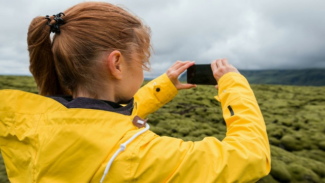 一名女性游客在一个有风的日子用智能手机拍摄绿色和长满苔藓的火山景观视频素材