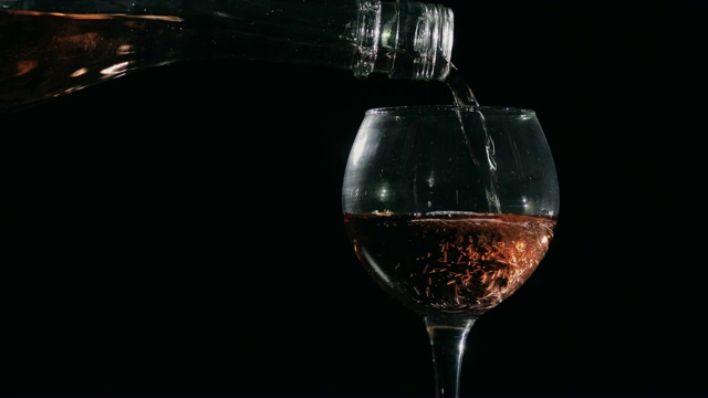 将玫瑰香槟从瓶中倒入玻璃杯中。黑色背景视频素材
