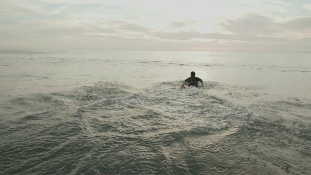 一个年轻人带着他的冲浪板跑进水里。视频下载