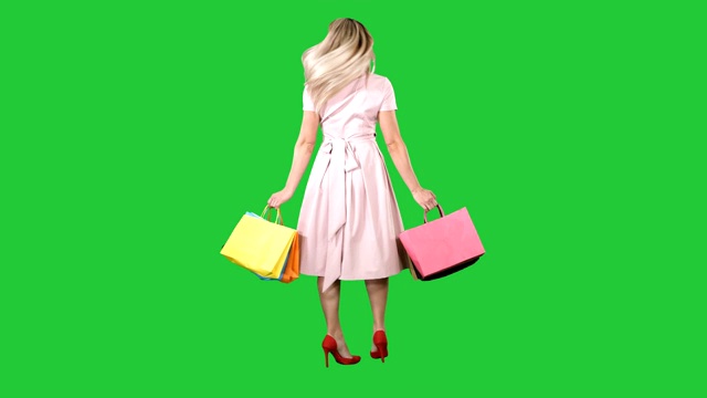 快乐的年轻女子转身，手里拿着购物袋看着绿色屏幕上的摄像头，色度键视频素材