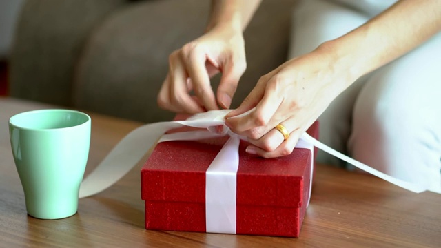 这个女人正在用白色丝带做一个红色礼品盒。视频下载