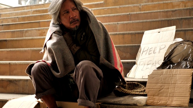 一个无家可归的老人穿着脏衣服坐在街上寻求帮助视频素材