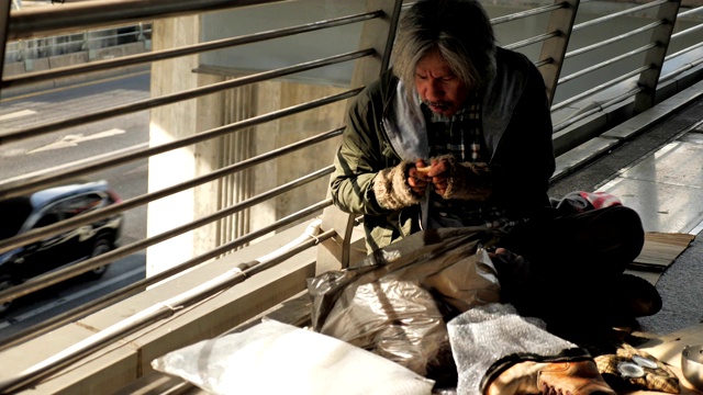 一个无家可归的老人穿着脏衣服坐在街上吃面包视频素材