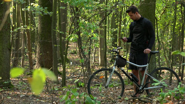 一个骑自行车的人站在森林里骑着自行车，用智能手机工作视频下载