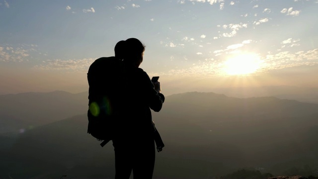 日落时分，徒步女子在山顶上用手机拍照，移动小车，慢动作视频素材