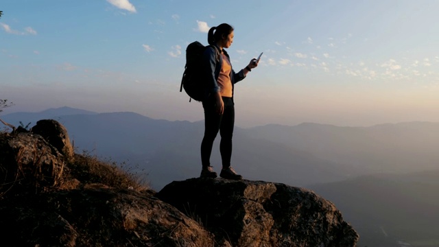 日落时分，徒步女子在山顶上用手机拍照，移动小车，慢动作视频素材