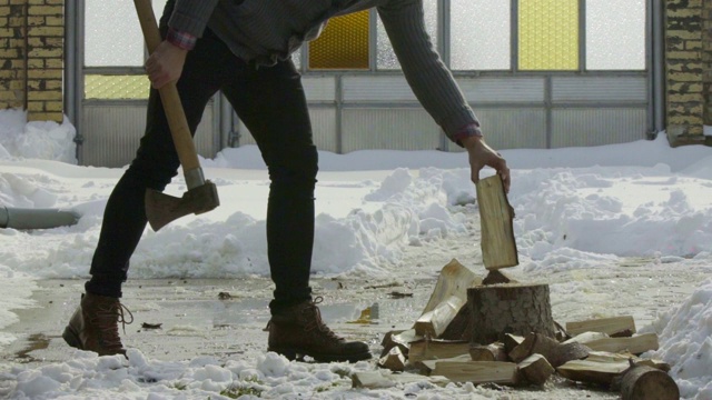 一个人在冬日村庄的雪院里砍柴的慢镜头视频素材