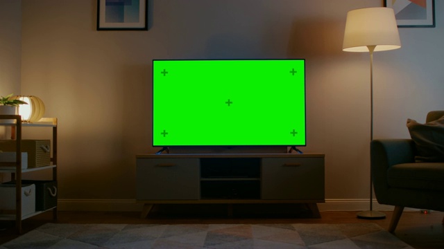 放大镜头与水平绿色屏幕模拟电视。舒适的夜晚客厅，家里有一把椅子和打开的灯。视频素材