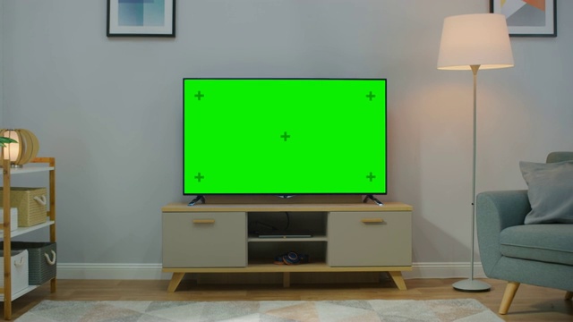 缩小镜头的电视水平绿色屏幕模拟起来。舒适的客厅白天与椅子和灯打开在家里。视频素材
