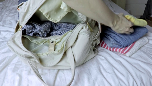 女人坐在床上，把衣服放进行李袋，准备旅行和旅行视频素材