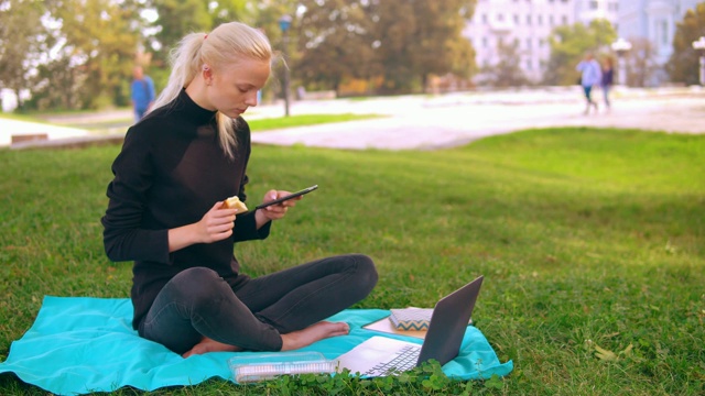 一个白人女孩在户外吃东西，在笔记本电脑上打字视频素材