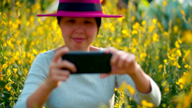 一名女子正走在夏日草地上，一边用手机拍照视频下载